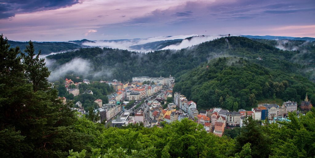 Karlovy-Vary - Blick auf die zwischen Hügeln liegende Stadt mit Wolken am Himmel